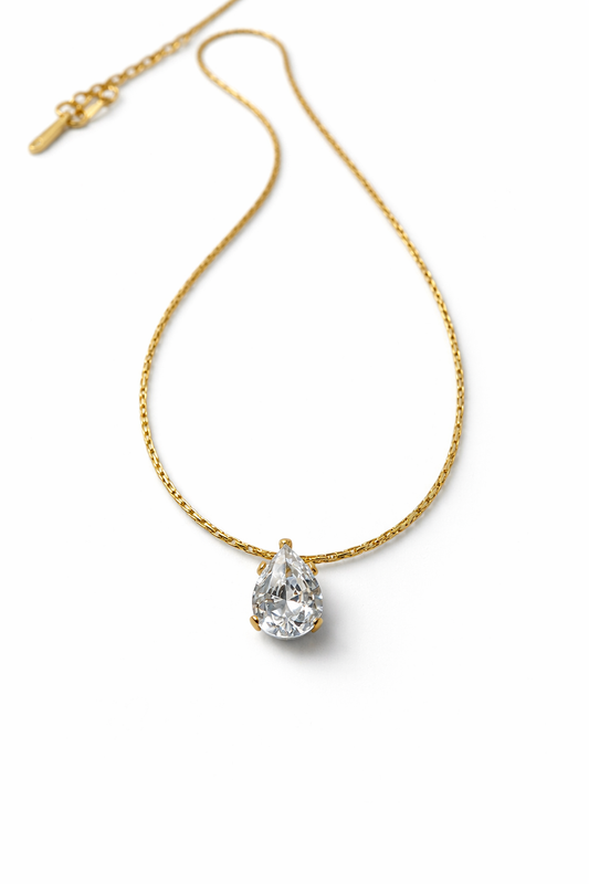 Gold necklace with a teardrop-shaped diamond pendant on a white background by Zenva