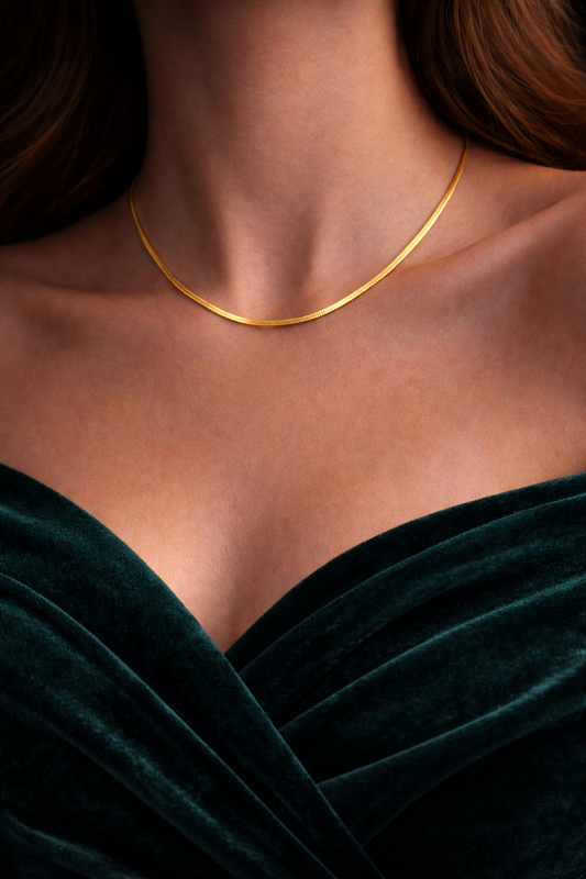 Gold necklace on a person wearing a dark green dress against a neutral background by Zenva